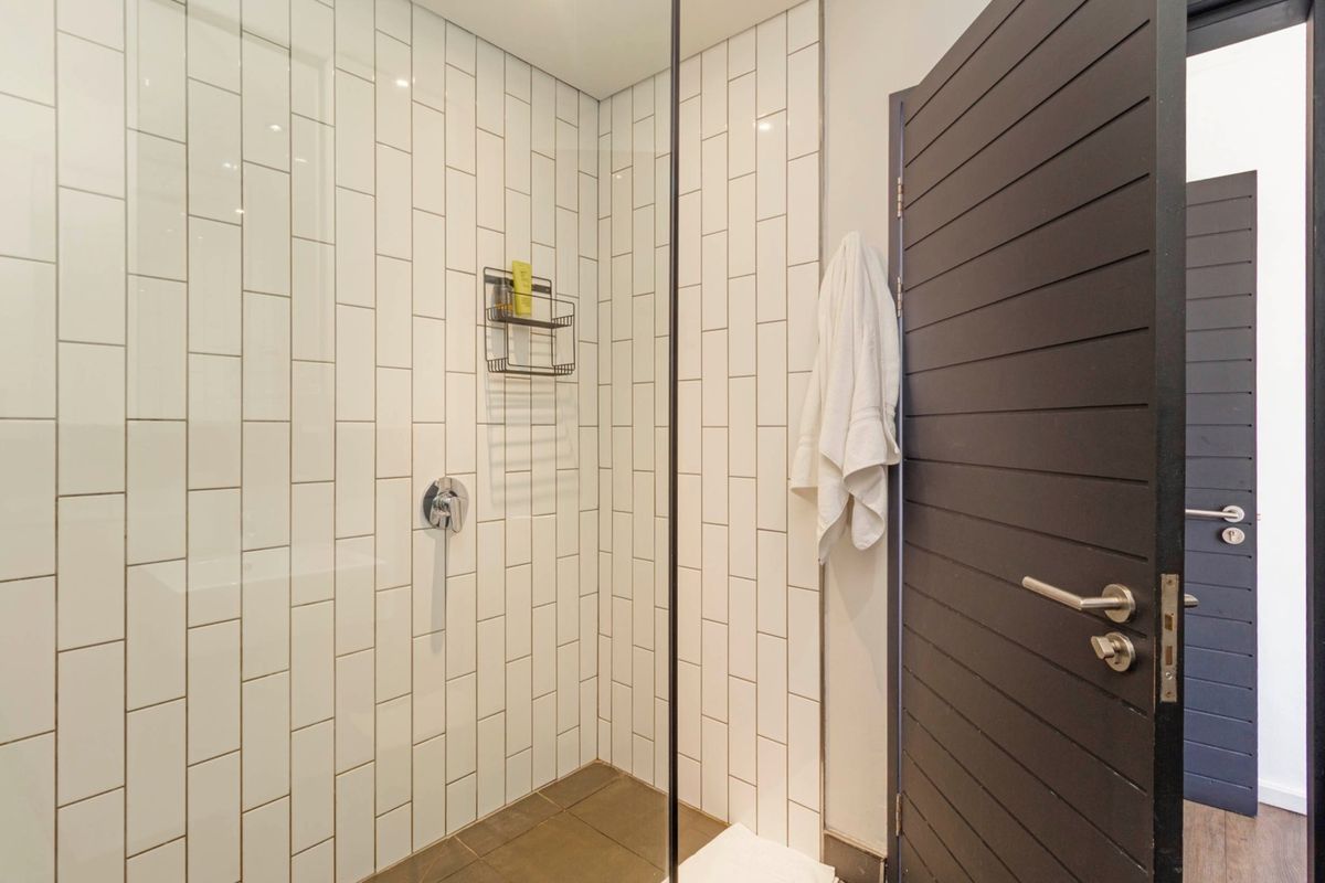 Modern bathroom featuring a walk-in shower with white subway tiles, a glass screen, and a dark timber door.