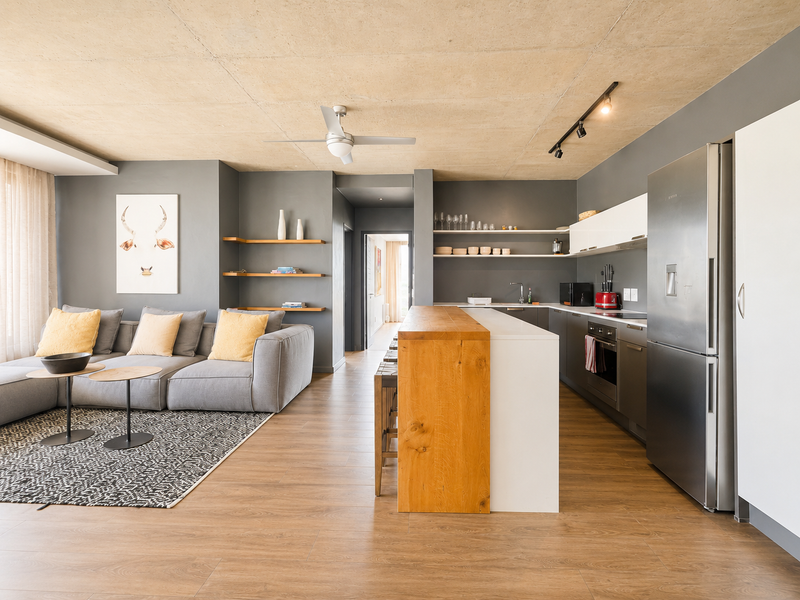 Modern open-plan living area featuring an exposed concrete ceiling, sleek kitchen cabinetry, a central island, and warm laminate flooring throughout.
