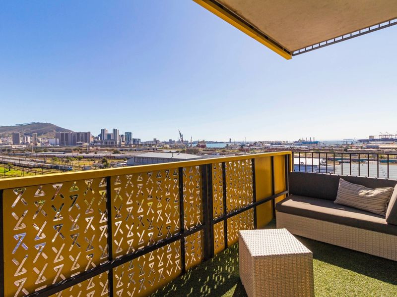 A private balcony featuring a decorative metal balustrade, artificial grass flooring, and an overhead awning, offering expansive city and harbour views.