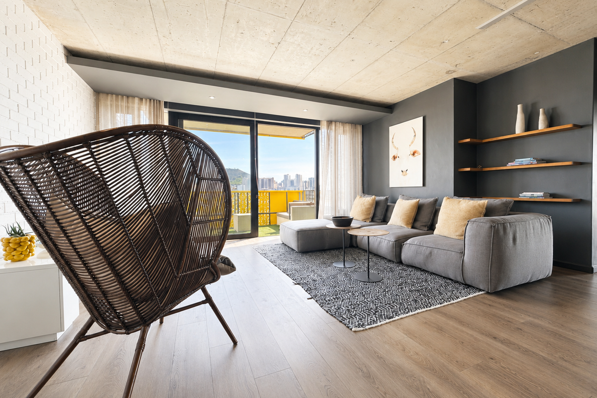 Modern living room featuring an exposed concrete ceiling, timber laminate flooring, built-in shelving, and large sliding doors opening to a balcony with city views.