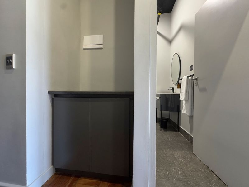 A clean hallway area featuring built-in cabinetry with a stone countertop, transitioning into a modern bathroom space with tiled flooring.