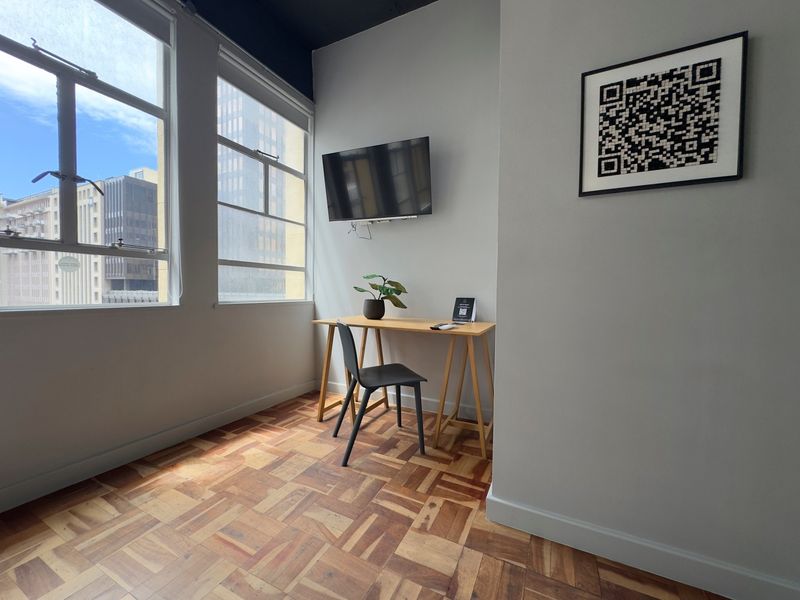 A bright office space featuring polished parquet flooring and large windows providing natural light and urban views.