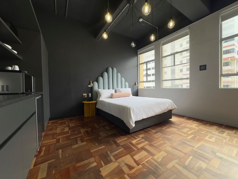 Modern bedroom featuring parquet flooring, exposed ceiling with pendant lighting, and built-in cabinetry, offering a contemporary urban aesthetic.