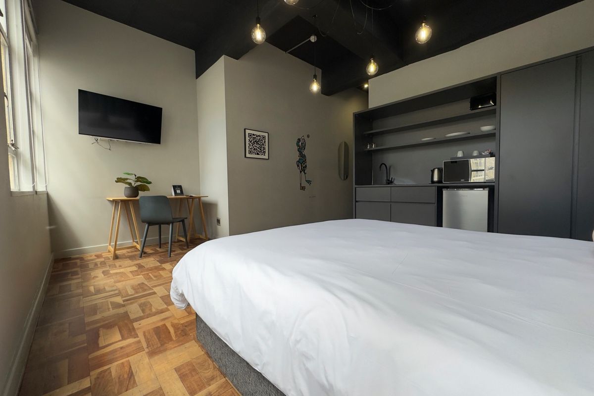 Modern bedroom featuring parquet flooring, exposed dark ceiling beams, and a compact built-in kitchenette area with integrated cabinetry and sink.