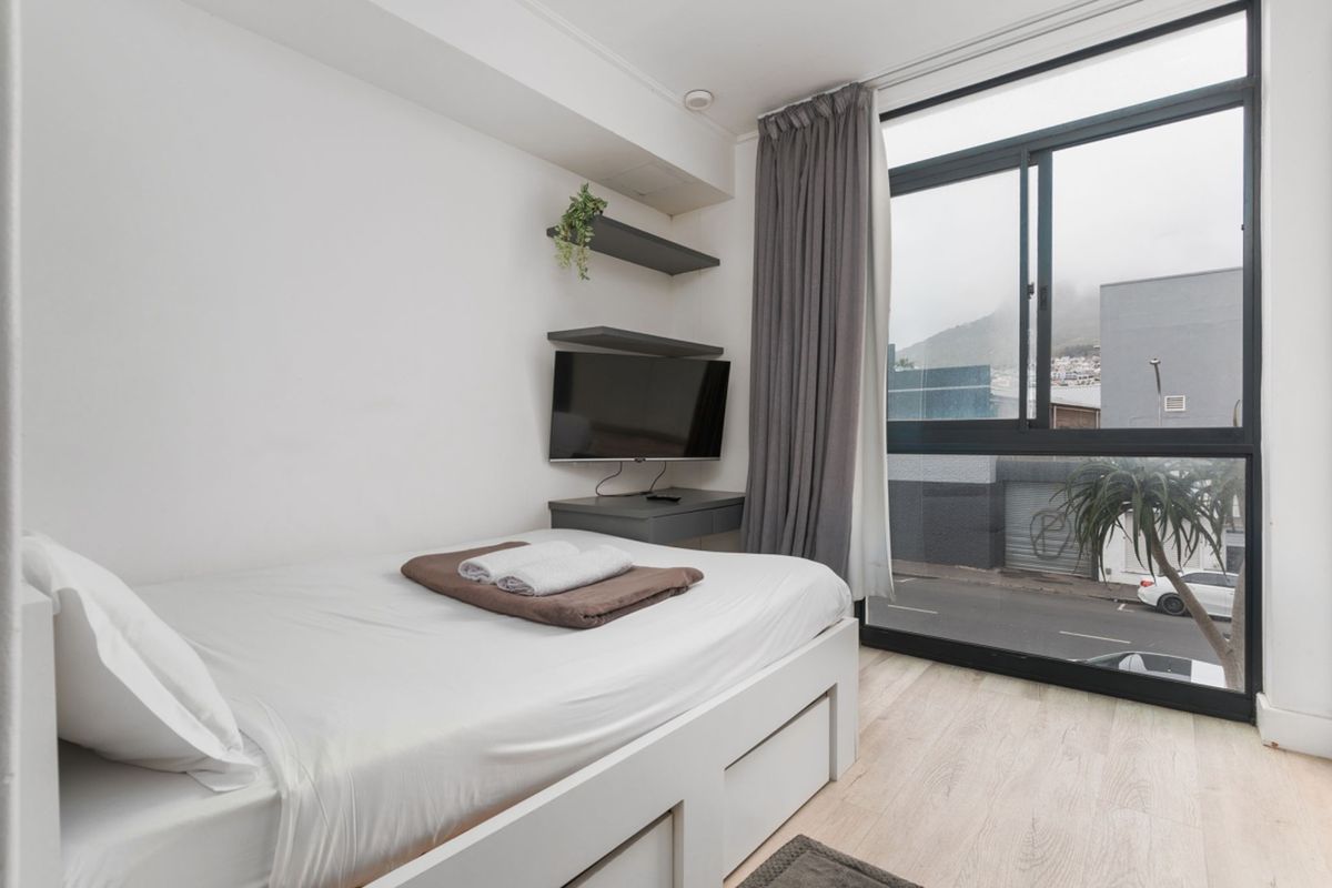 A bright bedroom featuring large floor-to-ceiling windows, modern laminate flooring, and built-in shelving units.
