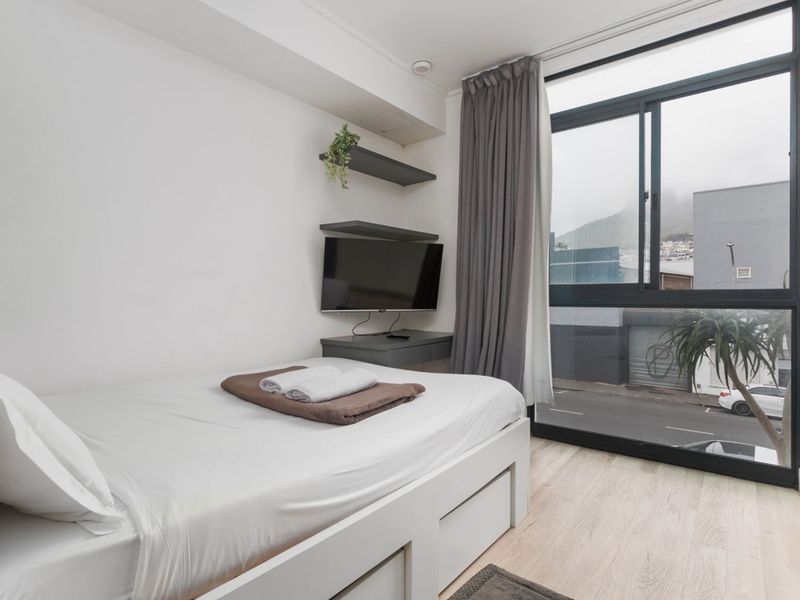 A bright bedroom featuring large floor-to-ceiling windows, modern laminate flooring, and built-in shelving units.