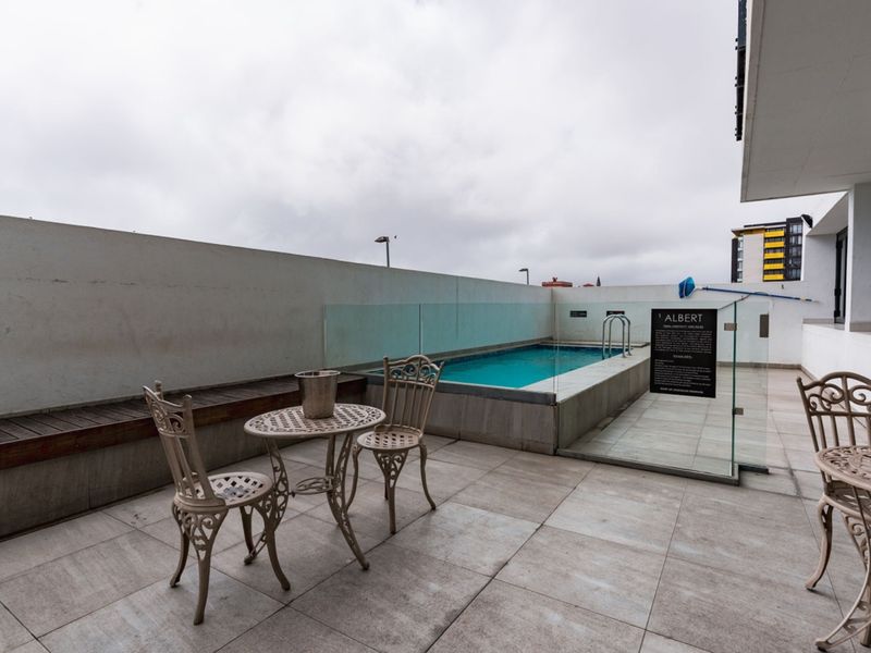 A modern rooftop pool area featuring a tiled deck, glass balustrades, and a built-in timber bench, offering a clean and functional outdoor space.