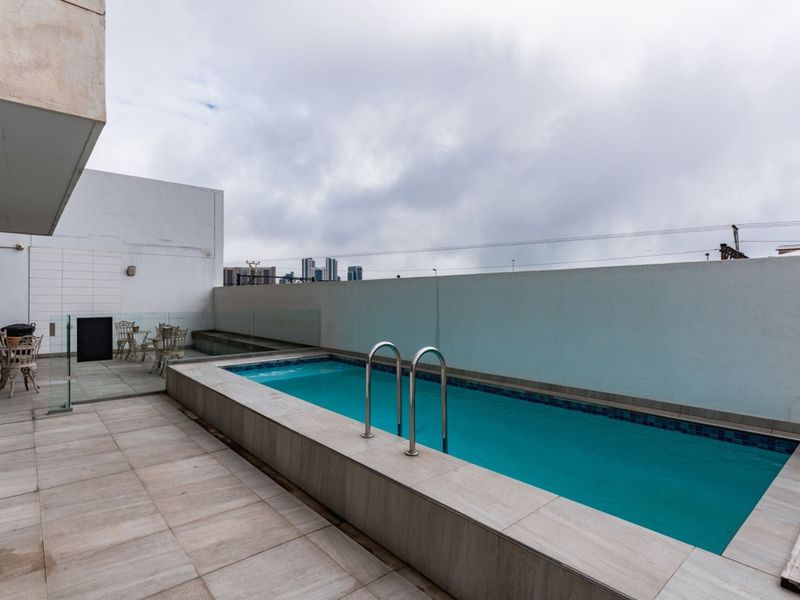 A private raised swimming pool area featuring tiled decking, a stainless steel ladder, and a glass balustrade, set against a high perimeter wall.