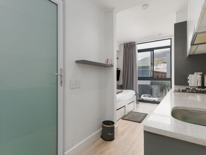 Modern open-plan studio apartment featuring a compact kitchen with stone countertops, gas hob, and integrated sink, leading into a bright bedroom area.