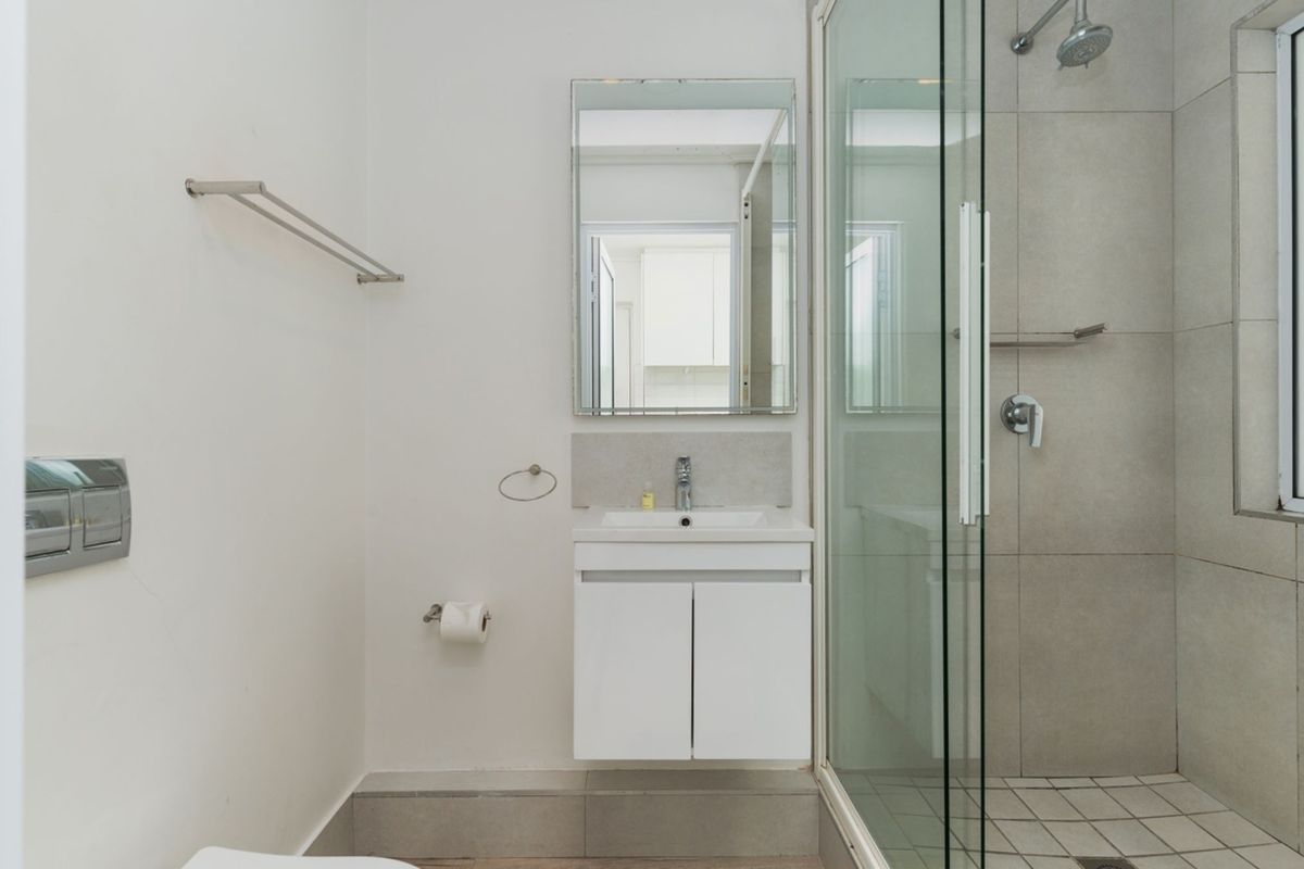 A clean, modern bathroom featuring a wall-mounted vanity, glass-enclosed shower with tiled finishes, and contemporary fixtures.