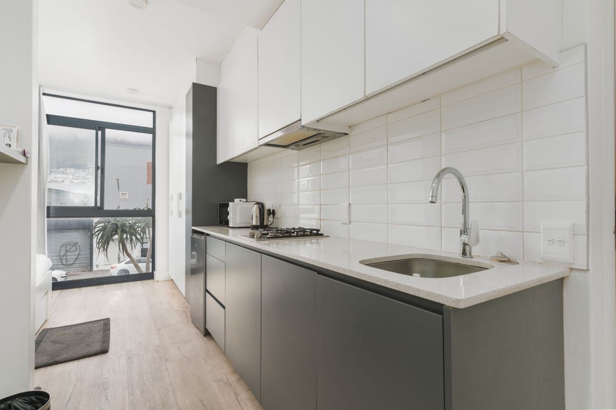 Modern galley-style kitchen featuring sleek two-tone cabinetry, stone countertops, a gas hob, and a subway tile backsplash with large window views.