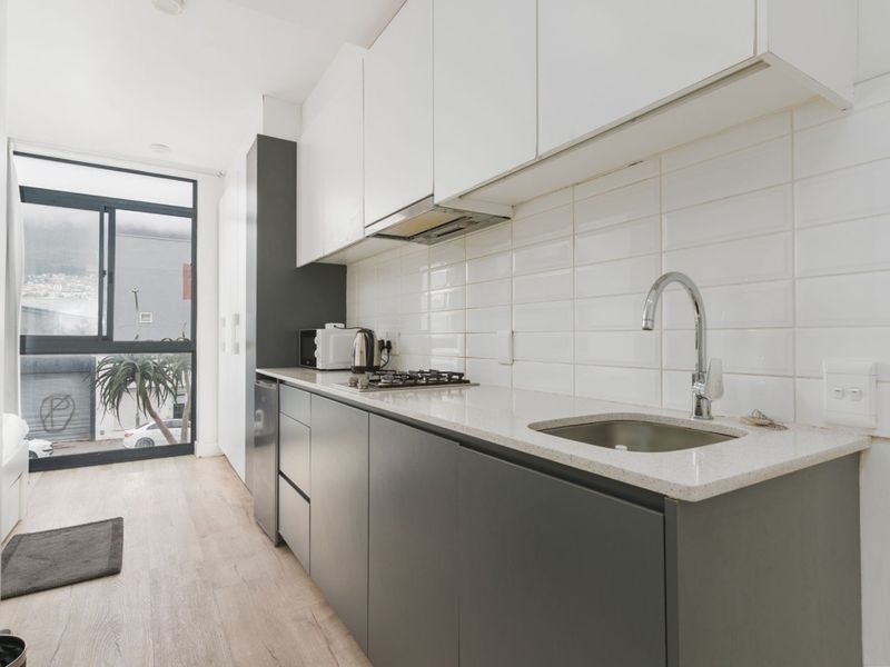 Modern galley-style kitchen featuring sleek two-tone cabinetry, stone countertops, a gas hob, and a subway tile backsplash with large window views.
