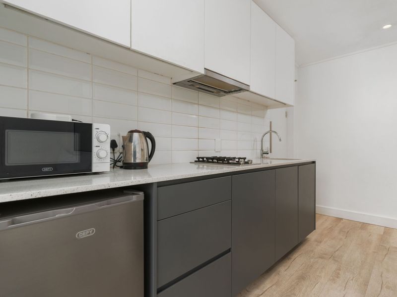 Modern compact kitchen featuring sleek grey lower cabinetry, white upper cabinets, stone countertops, gas hob, and a stylish subway tile backsplash.