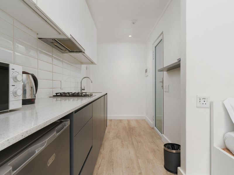 Modern galley-style kitchen featuring sleek dark cabinetry, stone countertops, subway tile backsplash, and a built-in gas hob with extractor fan.