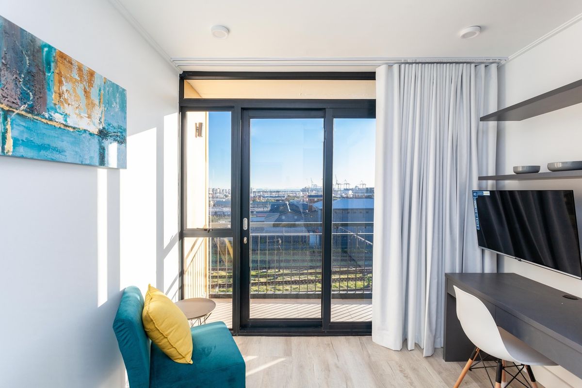 A bright bedroom featuring modern laminate flooring, built-in shelving, and a large sliding glass door providing access to a balcony with urban views.