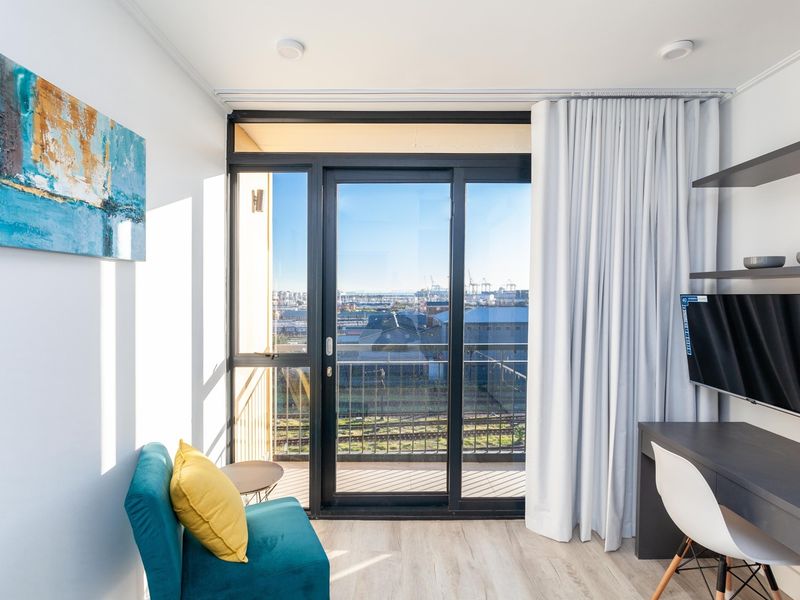 A bright bedroom featuring modern laminate flooring, built-in shelving, and a large sliding glass door providing access to a balcony with urban views.