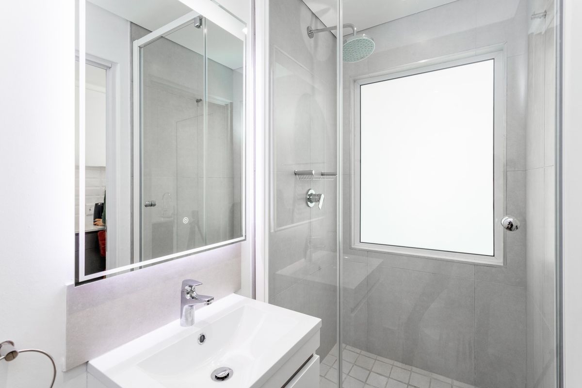 Modern bathroom featuring a sleek vanity basin, illuminated mirror, and a glass-enclosed shower with contemporary tiling and fixtures.