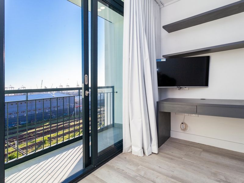 Modern bedroom featuring built-in desk and shelving, with a sliding glass door leading to a private balcony offering an industrial view.