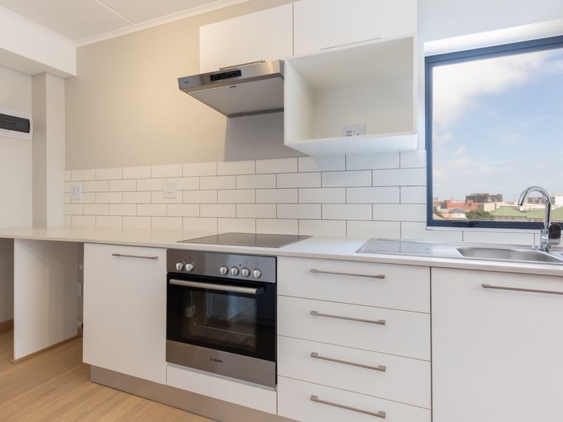 Modern kitchen featuring white cabinetry, subway tile backsplash, built-in oven, electric cooktop, and stainless steel sink with a view.