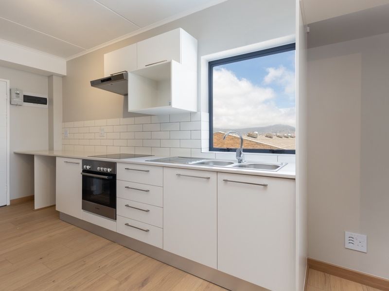 Modern, clean-lined kitchen featuring white cabinetry, subway tile backsplash, integrated oven and hob, and a stainless steel sink with a view.