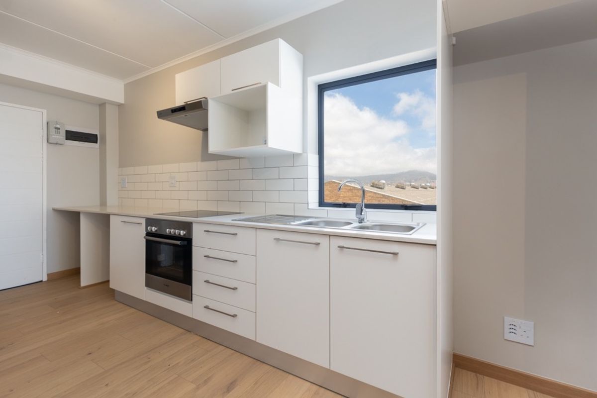 Modern, clean-lined kitchen featuring white cabinetry, subway tile backsplash, integrated oven and hob, and a stainless steel sink with a view.