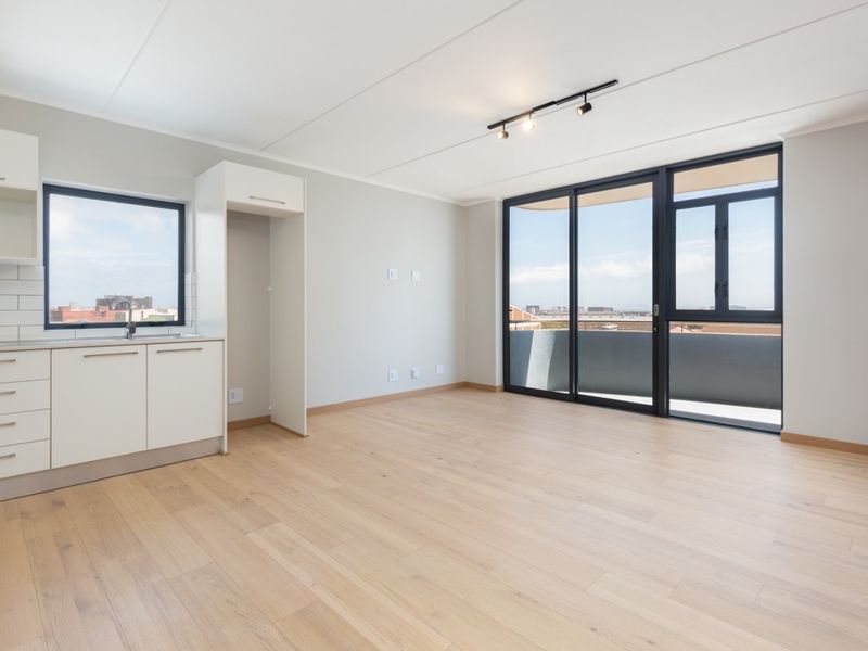 Bright open-plan living area featuring modern laminate flooring, a compact kitchen with built-in cabinetry, and large sliding doors leading to a private balcony.