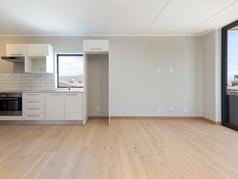 Modern open-plan living area featuring light wood flooring, a sleek kitchen with built-in appliances, and direct access to a balcony through a sliding door.