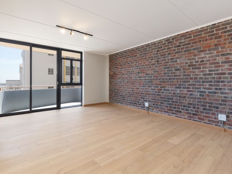 Bright and spacious living area featuring a striking exposed brick feature wall, light timber flooring, and large sliding doors leading to a private balcony.