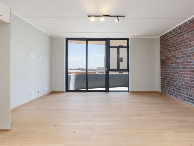 A bright, empty living room featuring modern laminate flooring, an exposed brick feature wall, and large sliding doors leading to a balcony.