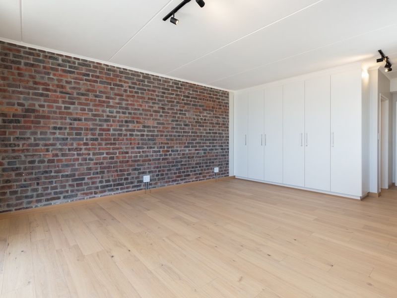 Spacious bedroom featuring a modern exposed brick accent wall, light laminate flooring, and extensive built-in storage cupboards.