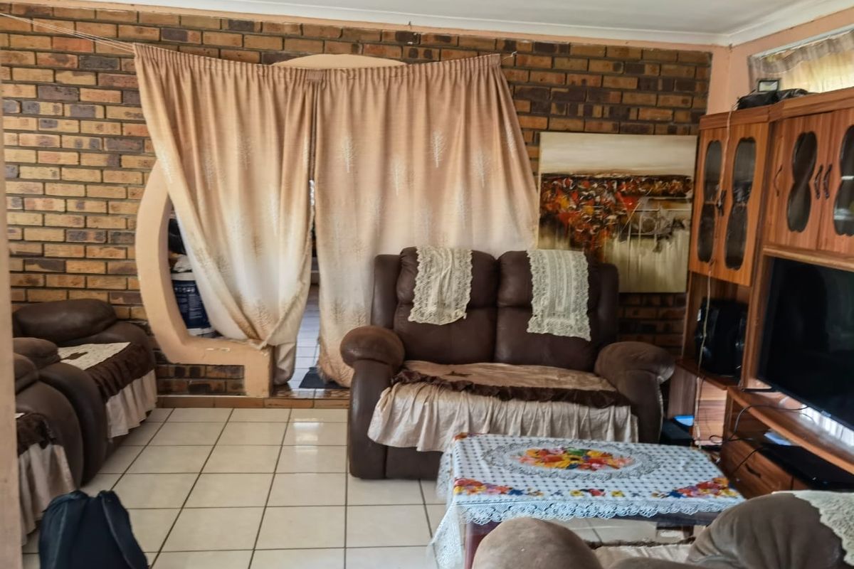 A living room featuring exposed face-brick walls, ceramic floor tiles, and a unique arched architectural opening leading to an adjacent space.