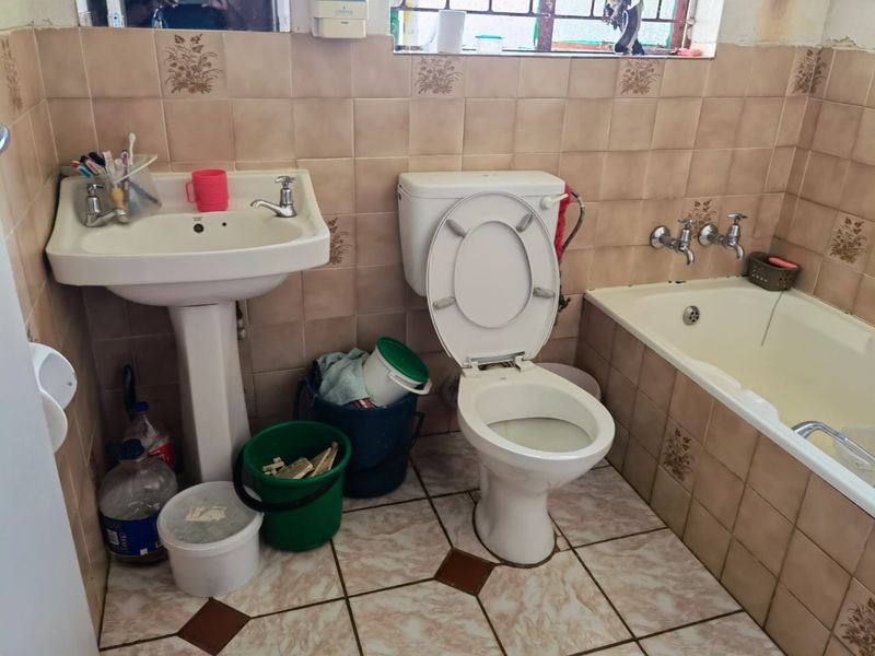 A dated bathroom featuring a pedestal sink, standard toilet, and built-in bathtub with wall-mounted taps and ceramic tiling throughout.