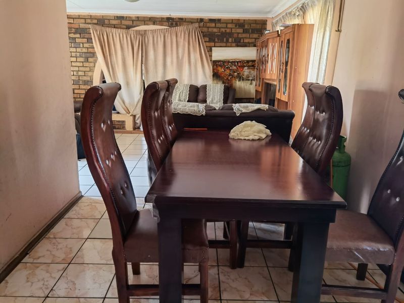 Open plan dining and living area featuring a rustic brick accent wall and tiled flooring throughout.