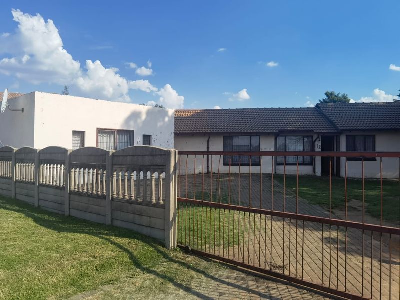 Front exterior view of a single-story house featuring a paved driveway, a metal security gate, and a precast concrete boundary wall.