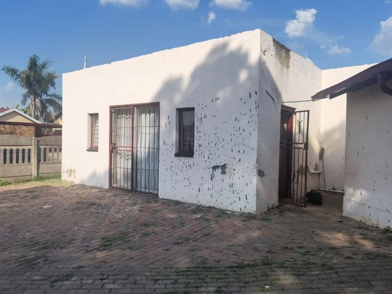 Exterior view of a detached structure featuring a paved courtyard, security gates, and weathered exterior wall finishes requiring maintenance.