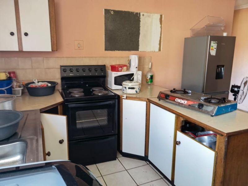 A functional kitchen featuring built-in cabinetry, a freestanding stove, and tiled flooring, requiring cosmetic updates to modernize the space.