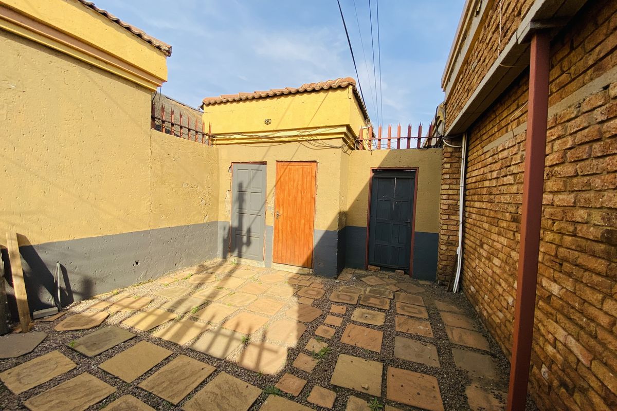 A rear courtyard area featuring paved flooring, exposed brick walls, and multiple access doors, requiring some maintenance and cosmetic updates.