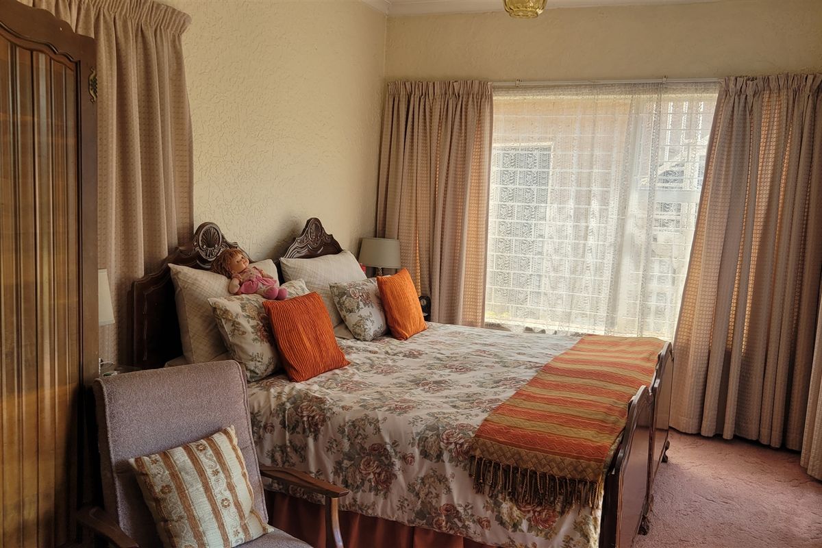 A bedroom featuring carpeted flooring, a built-in wardrobe, and large windows with curtains, offering a dated but functional living space.