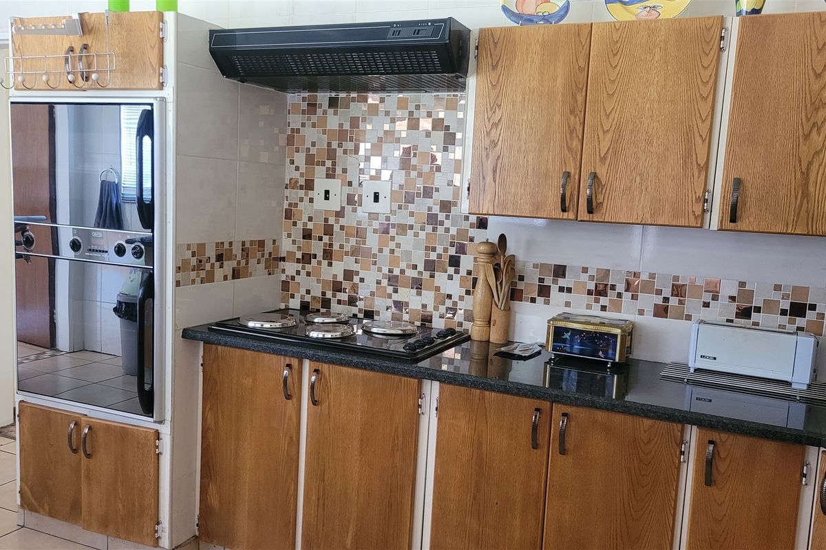 A functional kitchen featuring wood-finish cabinetry, granite countertops, a built-in oven, and a decorative mosaic tiled splashback.