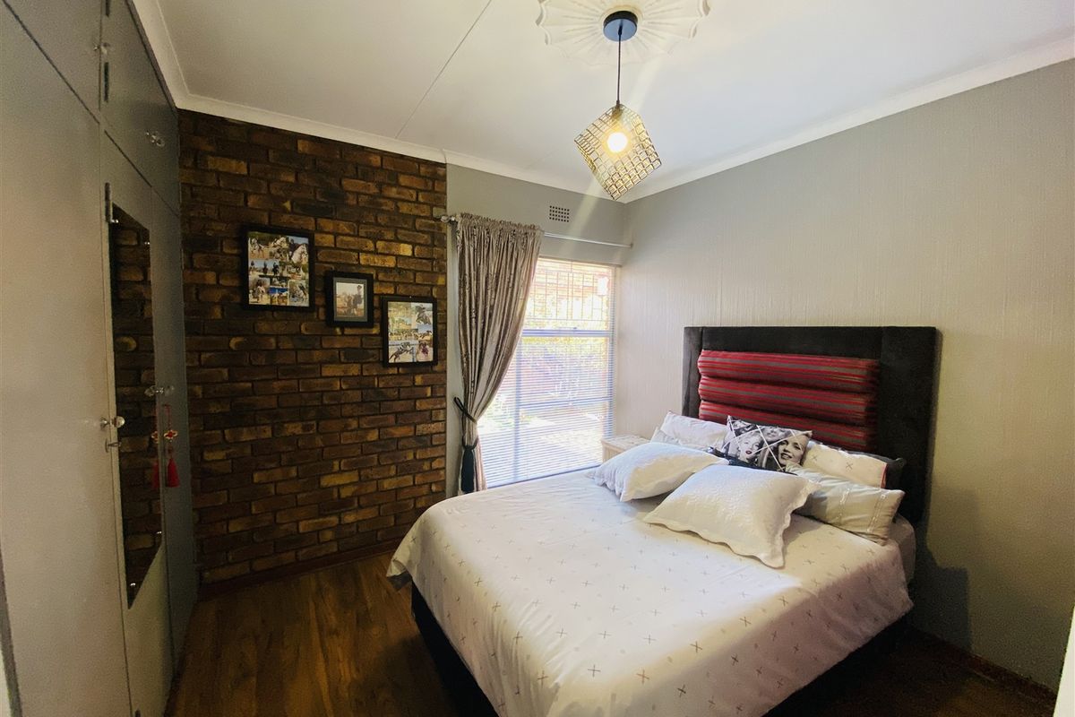 A well-maintained bedroom featuring an exposed brick accent wall, built-in cupboards, and a decorative ceiling rose with modern lighting.