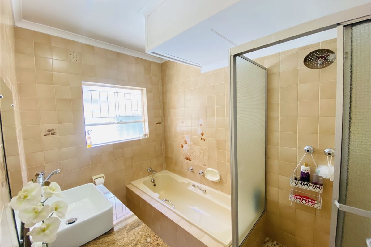 A functional bathroom featuring a built-in bathtub, separate shower enclosure, and a vanity basin set into a granite countertop with neutral wall tiling.