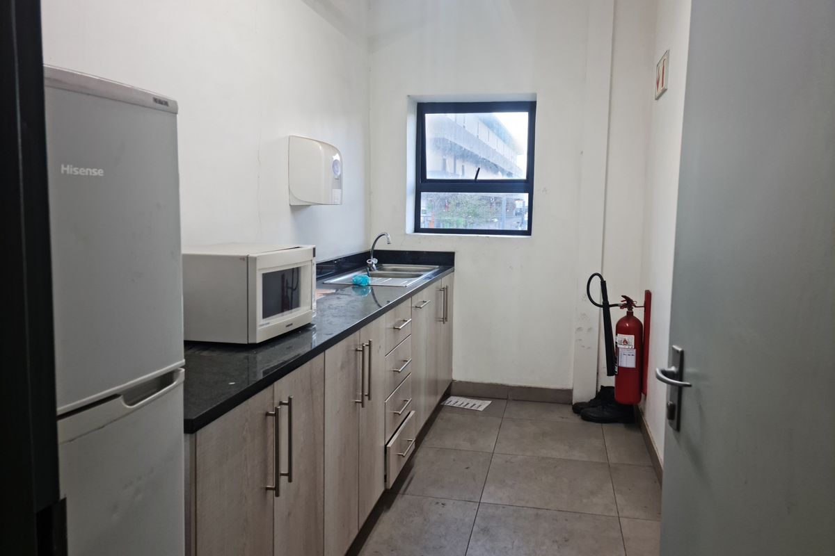 A functional industrial kitchenette featuring built-in cabinetry, granite countertops, a stainless steel sink, and tiled flooring.