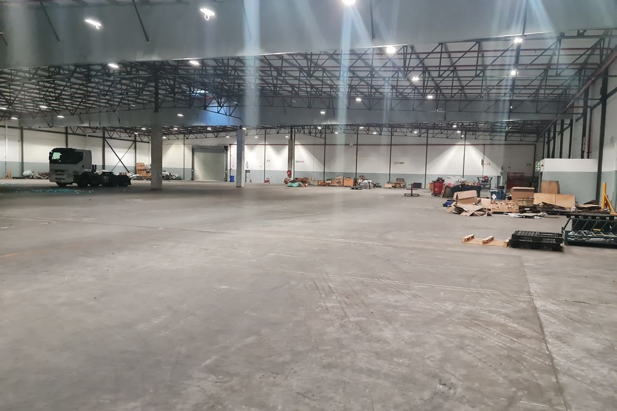 Spacious industrial warehouse featuring high ceilings with exposed steel trusses, concrete flooring, and a large roller shutter door for efficient logistics access.
