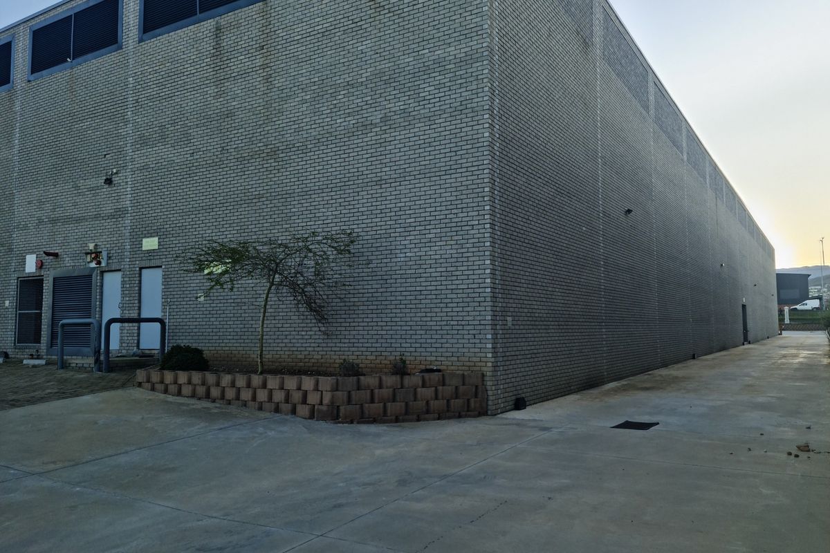 Side and rear view of an industrial warehouse building featuring a large brick facade, concrete driveway, and integrated ventilation systems.