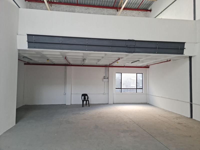 Spacious industrial unit featuring high ceilings with exposed steel beams, concrete flooring, and a fire sprinkler system, suitable for various commercial or storage uses.