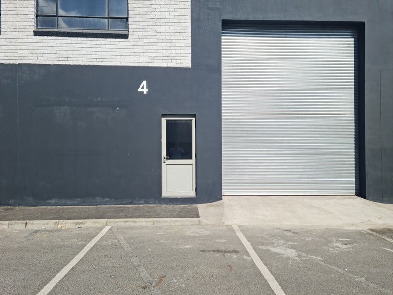 Industrial unit exterior featuring a large roller shutter door, separate pedestrian entrance, and dedicated asphalt parking bay.
