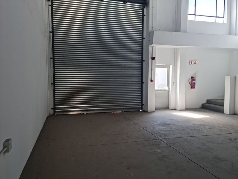 Spacious industrial utility area featuring a large roller shutter door, concrete flooring, and essential fire safety equipment.