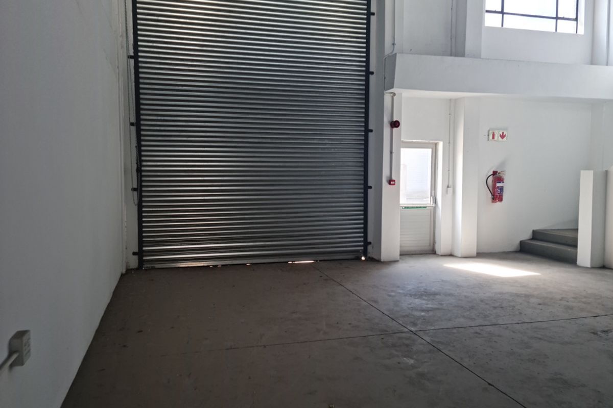 Spacious industrial utility area featuring a large roller shutter door, concrete flooring, and essential fire safety equipment.