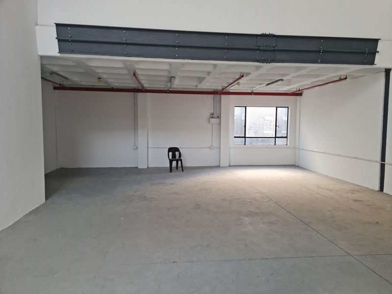 Spacious industrial utility area featuring exposed steel structural beams, waffle slab ceiling, fire sprinkler system, and polished concrete flooring with natural light.
