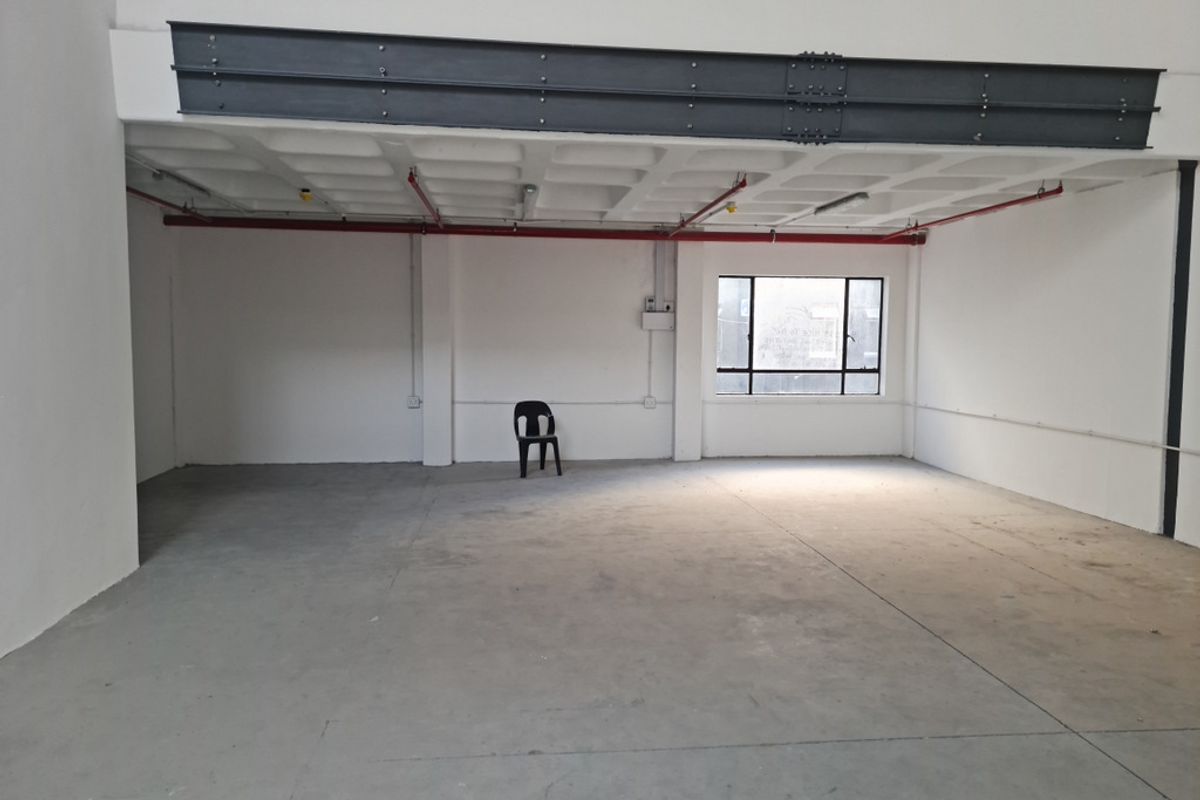 Spacious industrial utility area featuring exposed steel structural beams, waffle slab ceiling, fire sprinkler system, and polished concrete flooring with natural light.